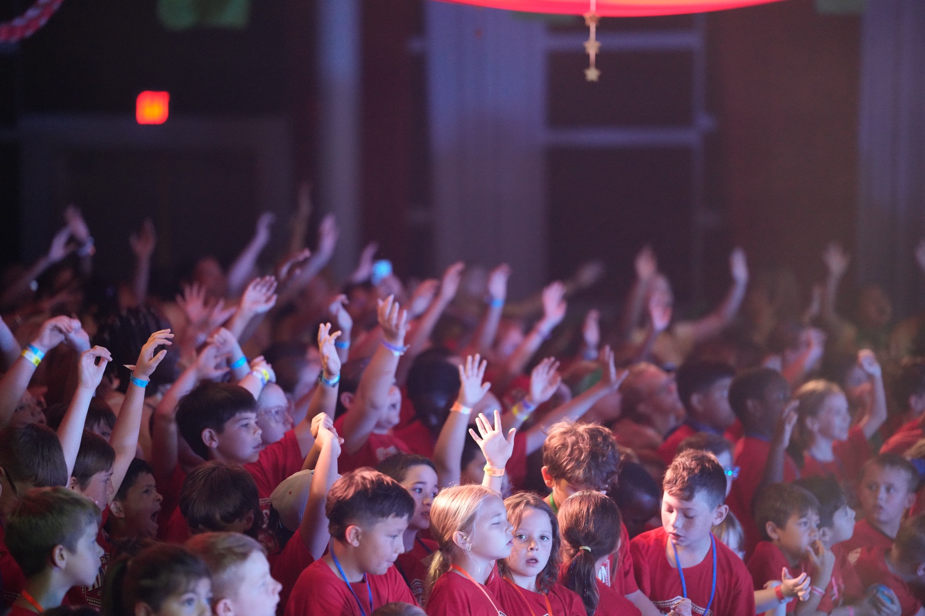 A room full of kids with hands raised in worship at KidCon